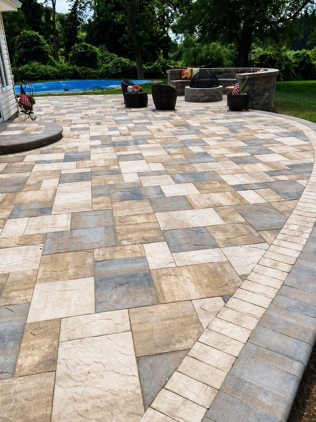 Elevated paver patio beside a swimming pool with landscaped surround.