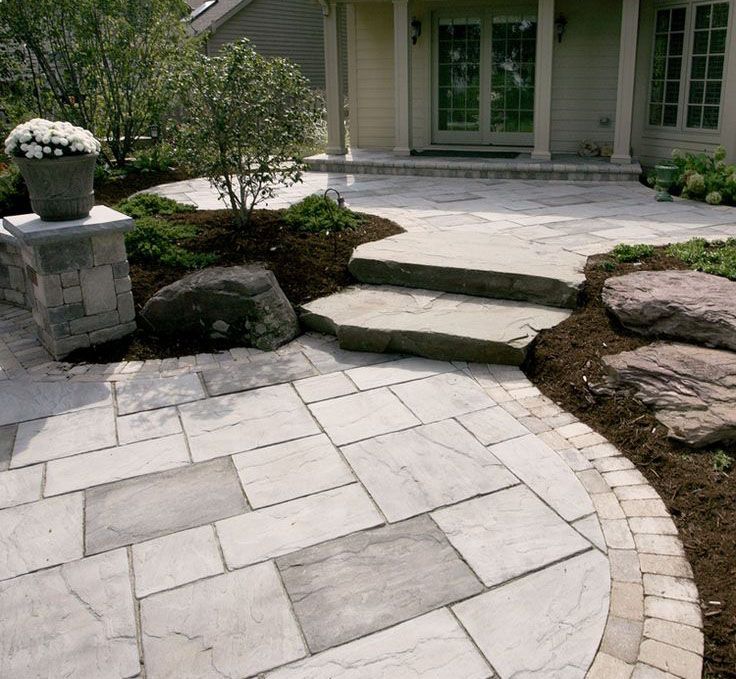 Circular paver patio with wide stone tread steps rising through a landscaped garden bed.