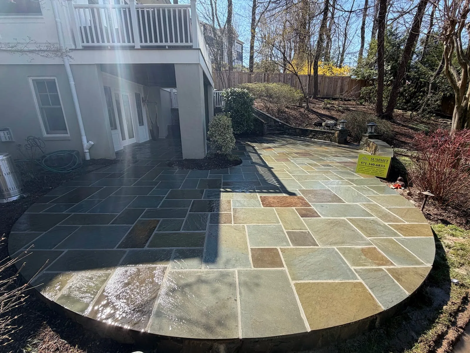 Large semicircular bluestone patio with mixed gray and tan flagstones under a deck