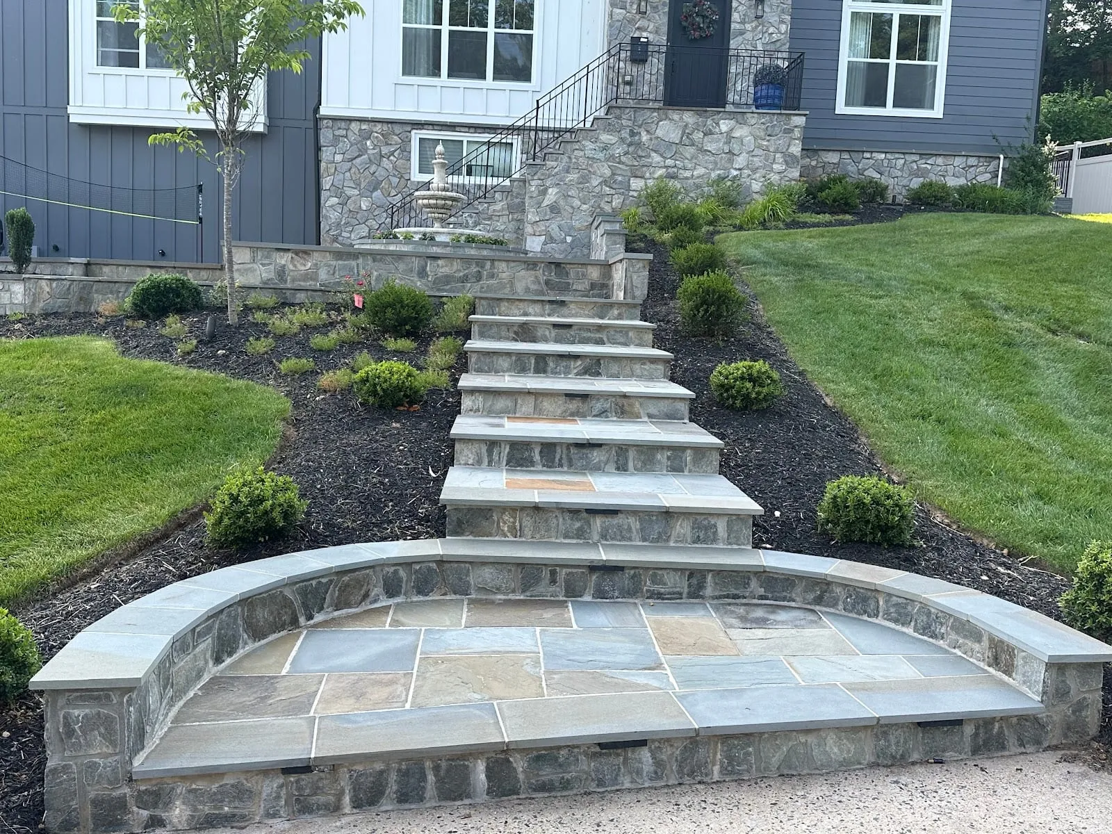 Curved bluestone seat-wall landing with steps rising to a stone-faced home