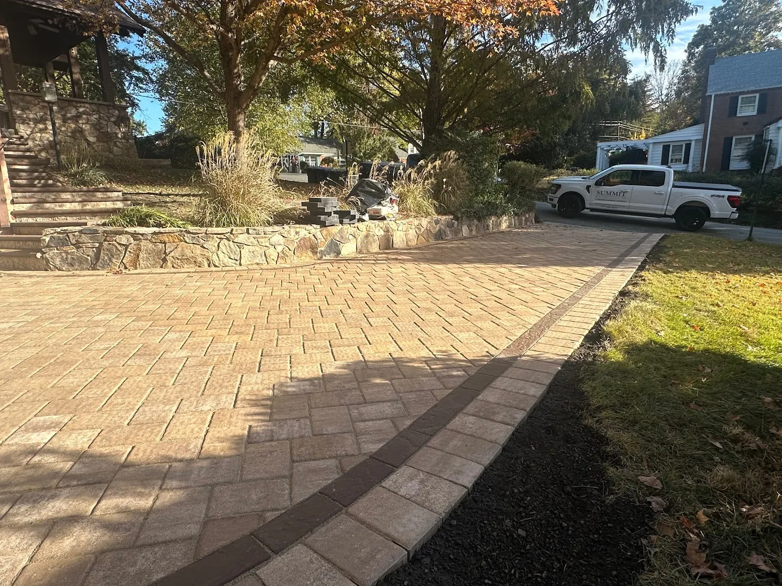 Tan paver driveway at golden hour past stacked-stone retaining wall