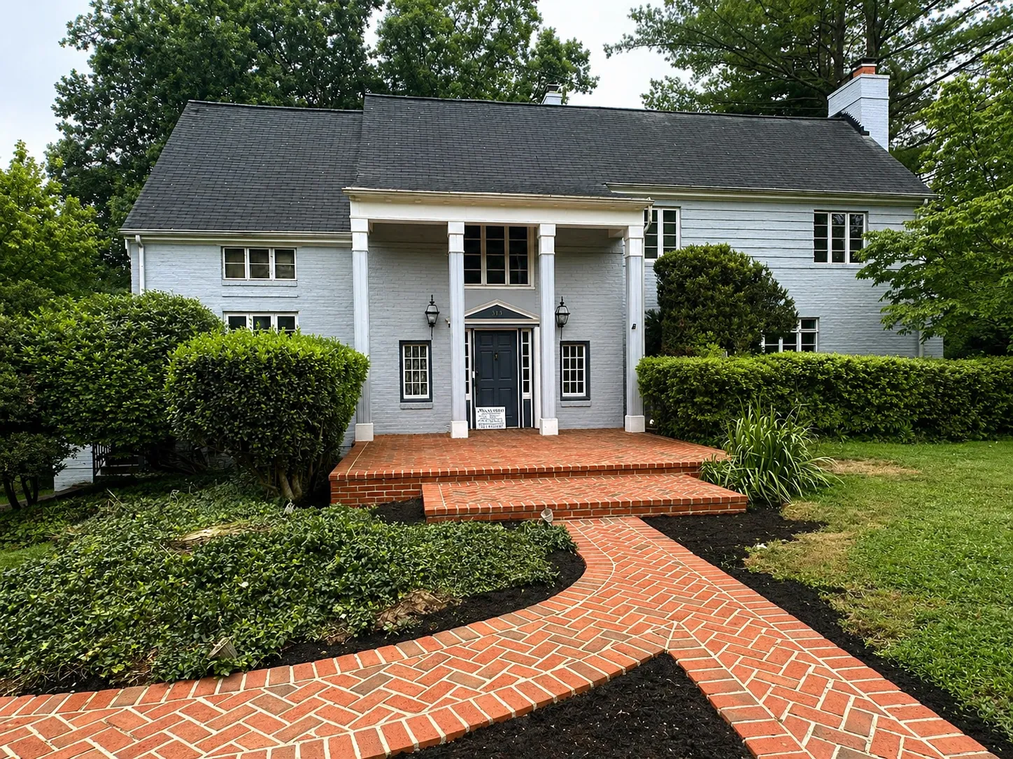 Herringbone brick walkway leading to a brick-clad colonial home with twin-column portico.