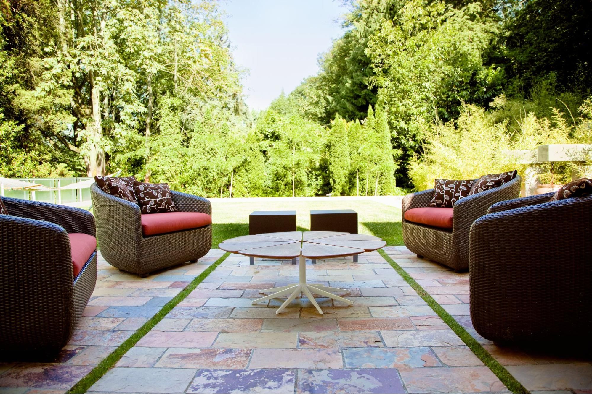 Hand-set flagstone patio framed by dark wicker lounge chairs with red cushions and a low round table, surrounded by deep greenery.