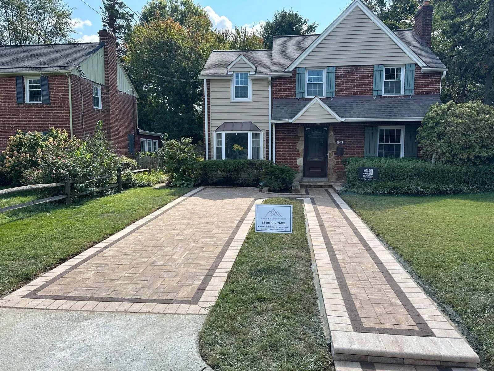 Multi-tone tan and charcoal paver driveway with red brick banding, gray colonial home, Summit yard sign in foreground
