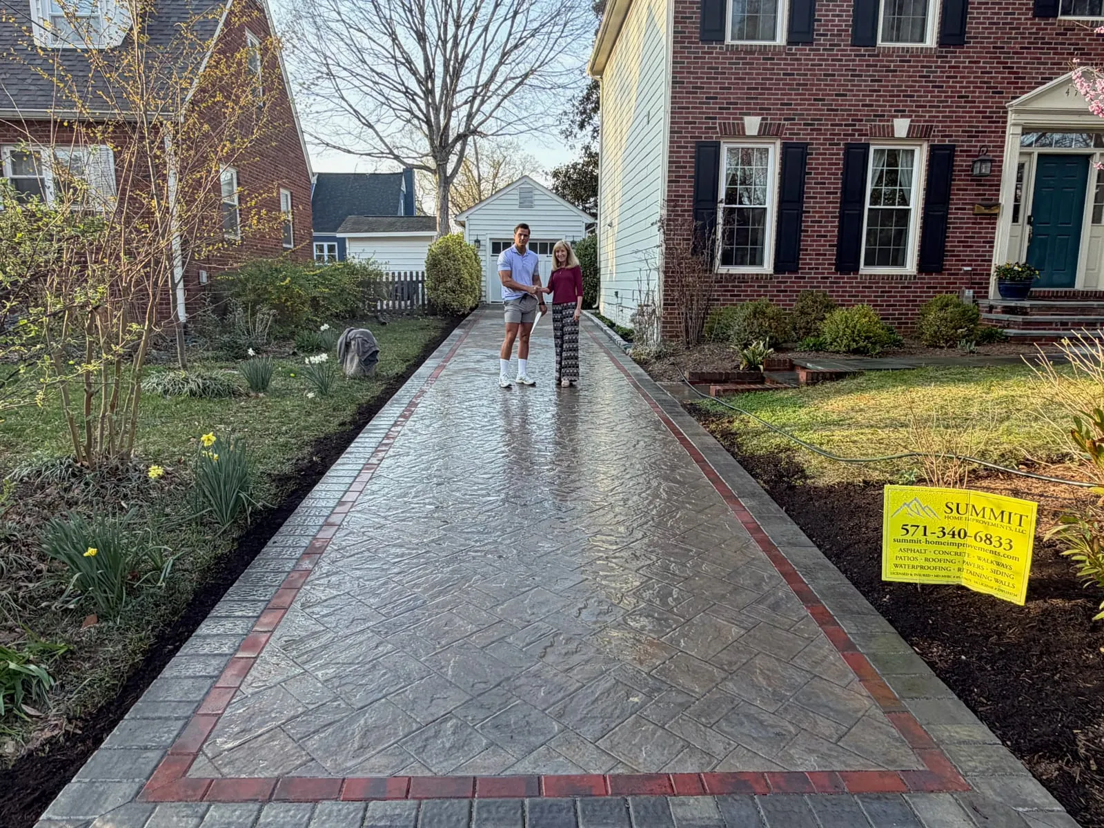 Stamped-stone driveway with red brick herringbone border at a brick colonial
