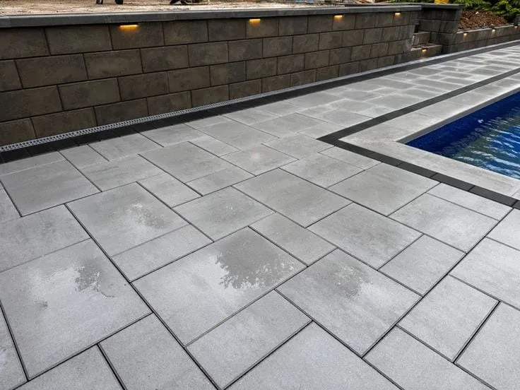 Large-format gray paver pool deck with charcoal block retaining wall