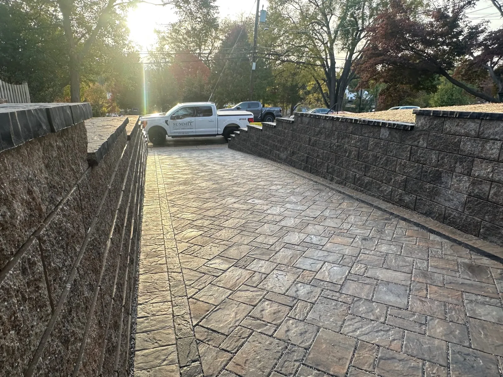 Backlit cobblestone-pattern paver drive between block walls at golden hour