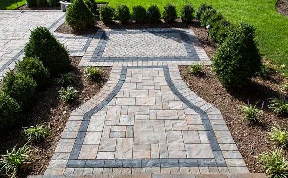 Formal paver walkway bordered by landscaped planting beds and a stone curb.