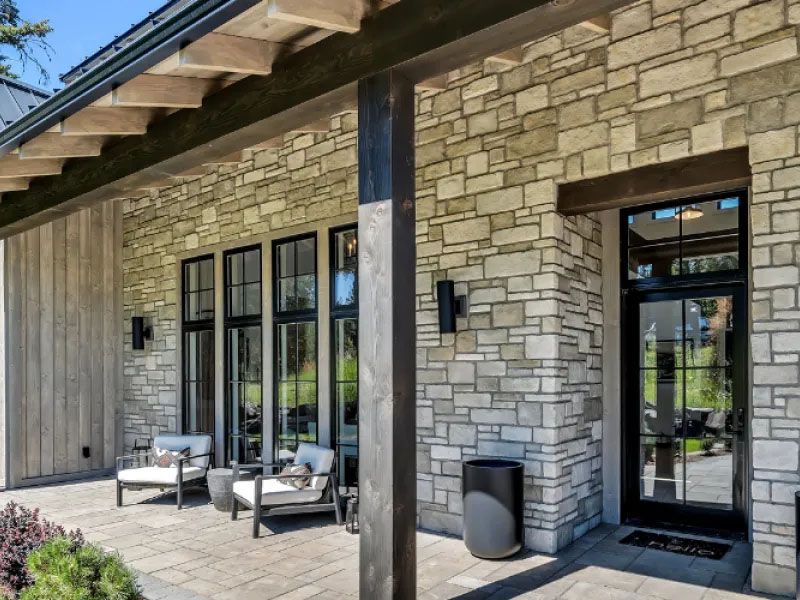 Modern home with gray stacked-stone veneer and fabric canopy over a paved terrace.