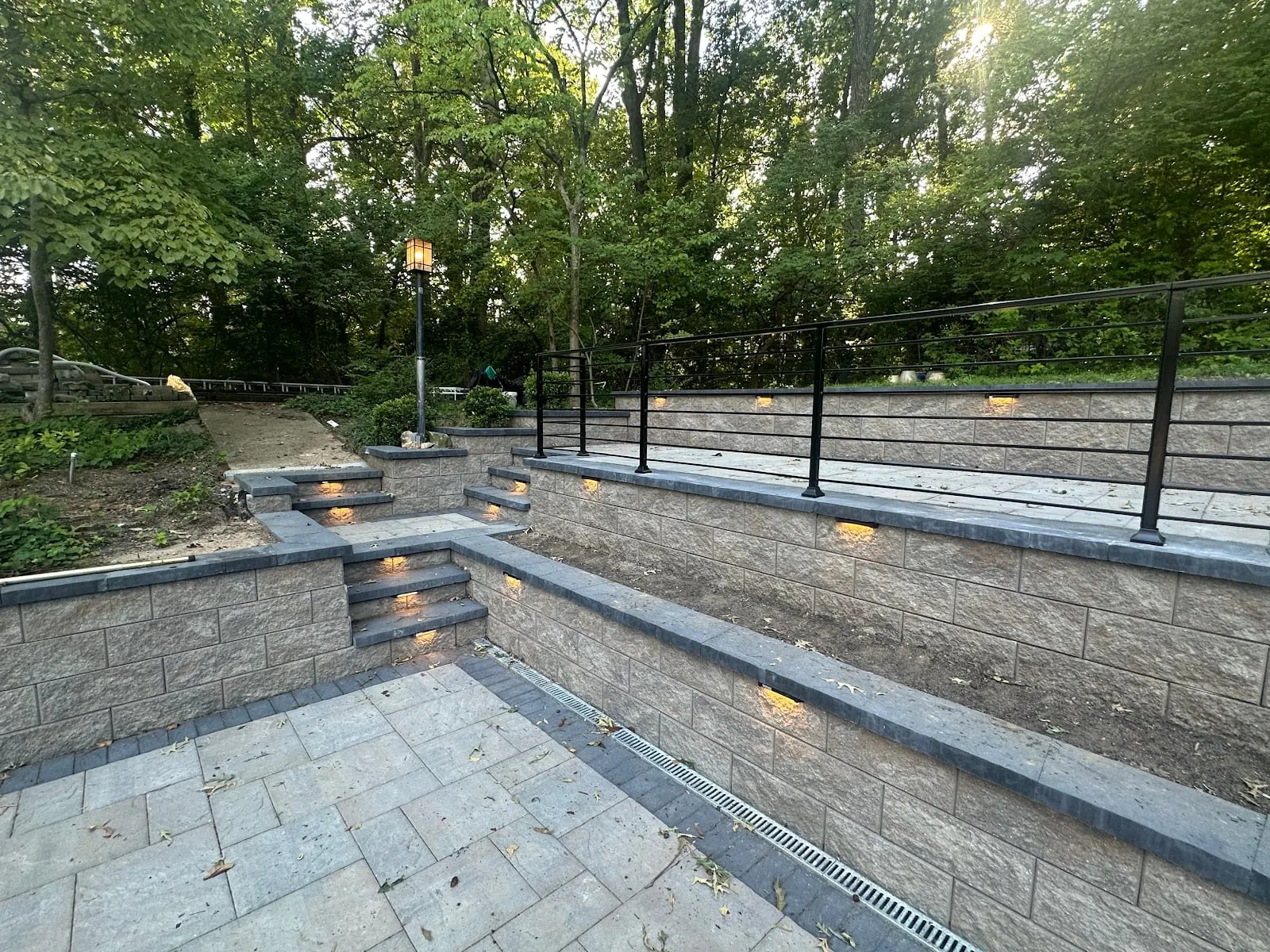 Two-tier charcoal block retaining wall with metal railing and step lights