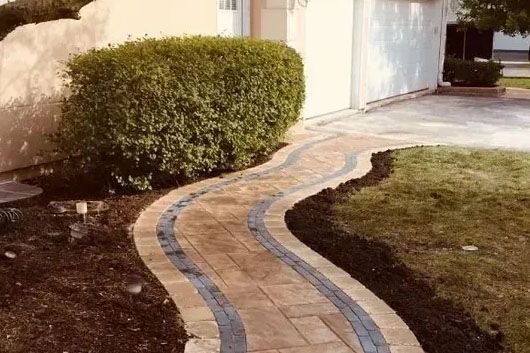 Curved hand-set clay paver walkway winding through a planted garden bed.